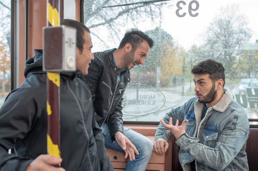 Three men sharing a laugh inside a tram. Photo.