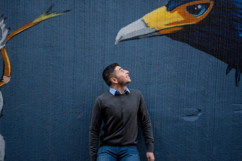 A man looking up at a large bird on a mural/street art. Photo.