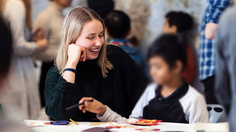 A smiling female student sitting togehter with a child. Photo.