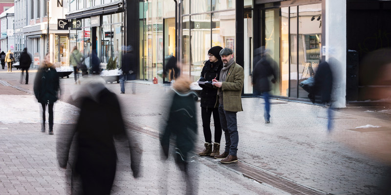 Two people standing in a street watching people walking by. Photo.