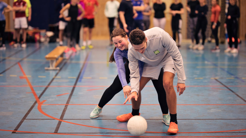 Two studentes playing handball in a sports hall. Photo.