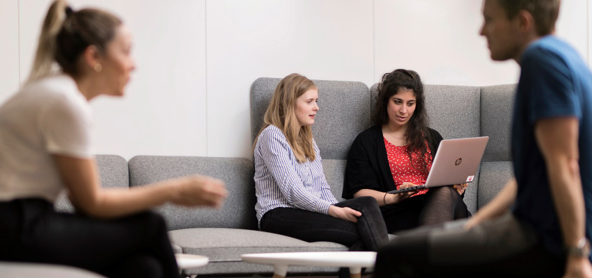 Students talking and sitting in fron of a pc. Photo.