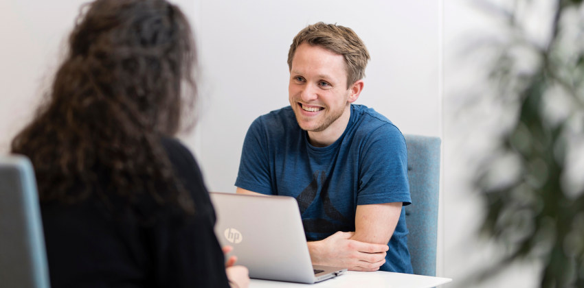 Two people talking together. One of them has a computer in front of them. Photo