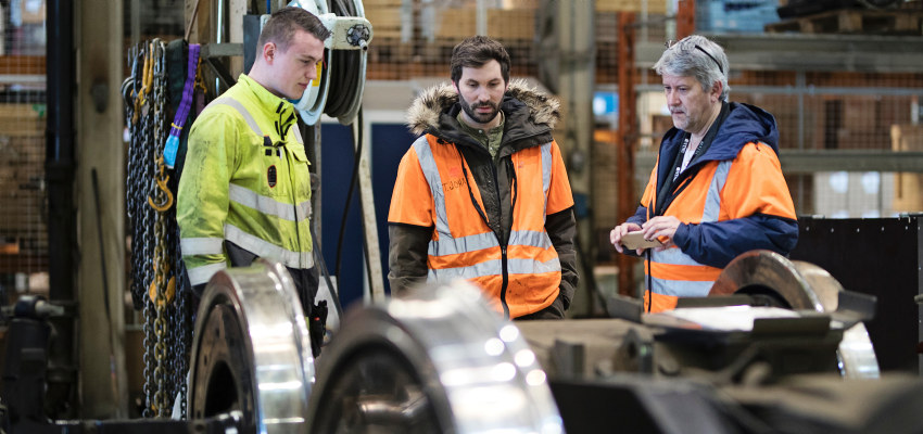 Three people looking at train wheels. Photo.