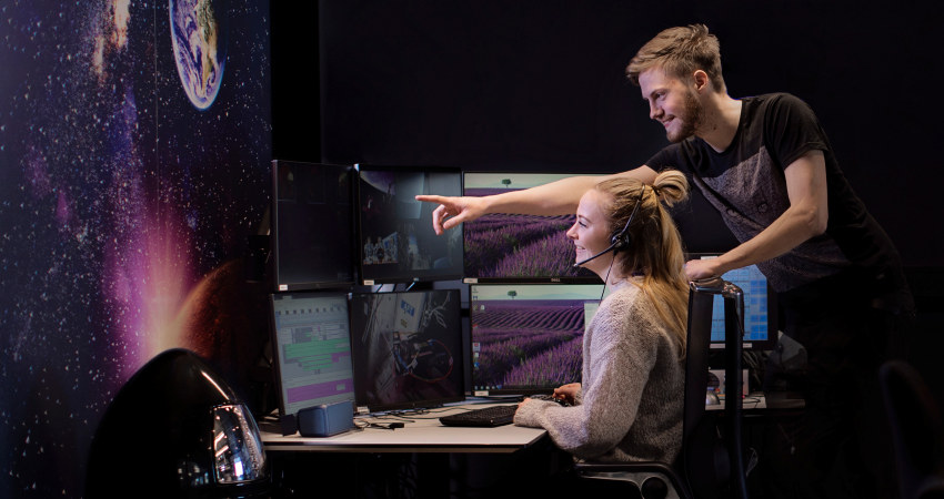 Two people are looking at a PC screen in a space control room. Photo.