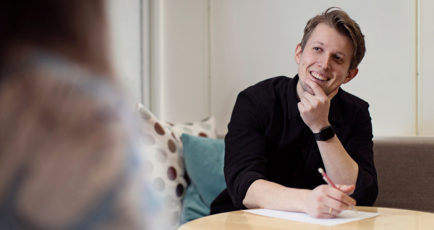 Person som sitter ved et bord og smiler. Foto.