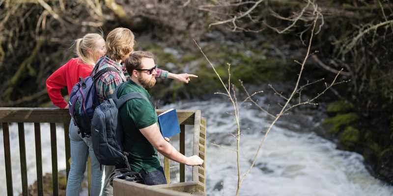 Three people looking at a waterfall. Photo.