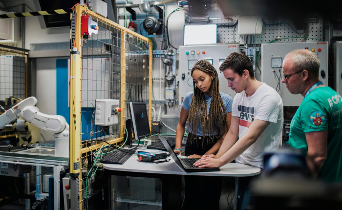 To elever og en lærer jobber med maskin på elektro. Foto