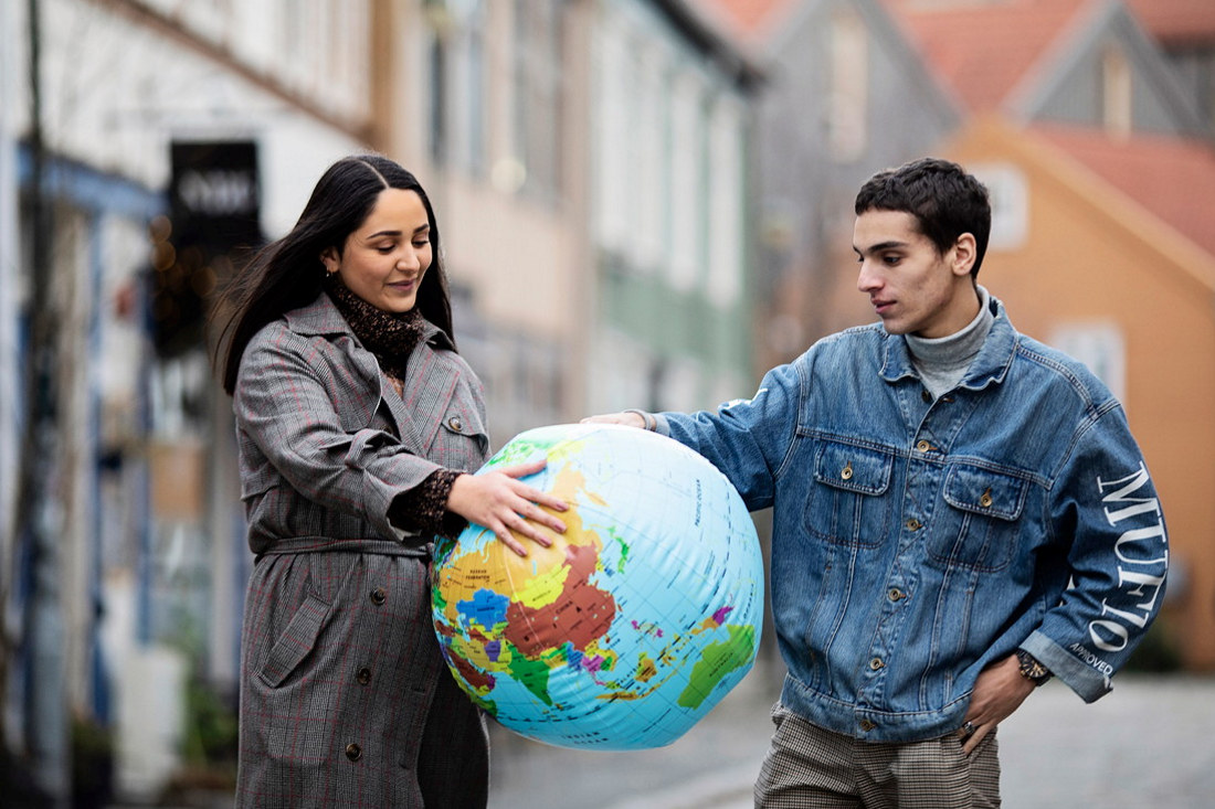 To studenter står i en gate og holder i en stor globus som de ser ned på. Foto.