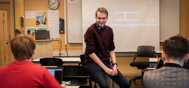 Lærerstudent i klasserom. Smiler til elever. Foto.