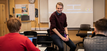 Student snakker med elever i et klasserom. Foto.