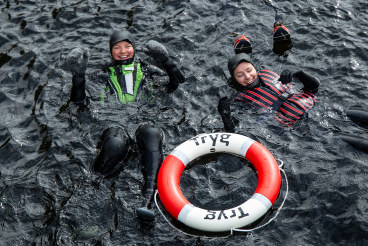 To studenter med våtdrakt og Tryg-ring i vannet. Foto