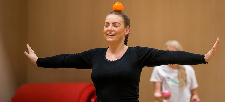 Kvinne med armene ut til siden og en oransje kule på hodet. Foto