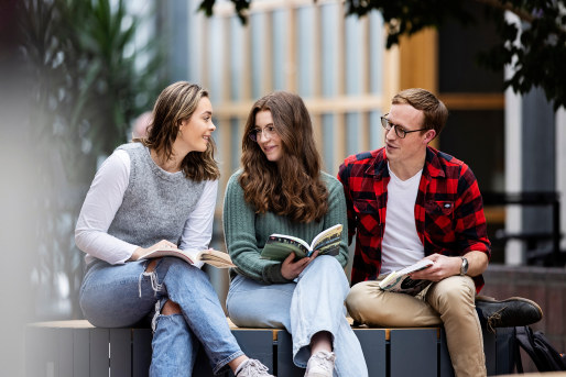 Tre studenter sitter sammen med bøker i hendene. Foto