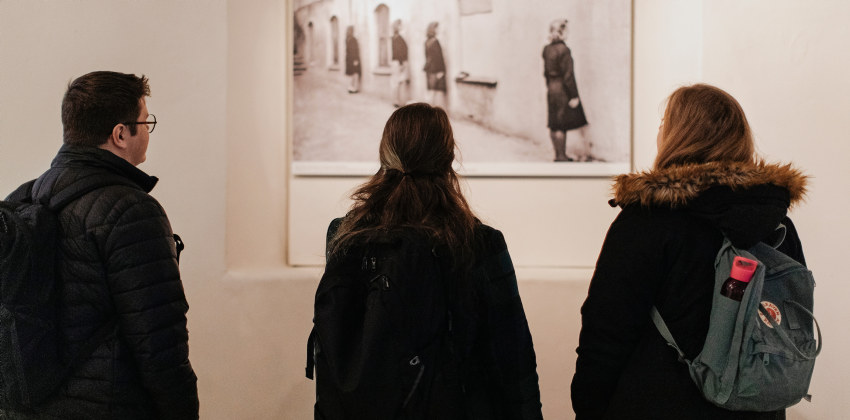 Tre studenter, en mann og to kvinner, står med ryggen til og ser på et stort svart-hvitt fotografi fra Justismuseet. Foto