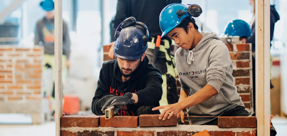 Two students, boys, in construction work together to build a wall. Photo