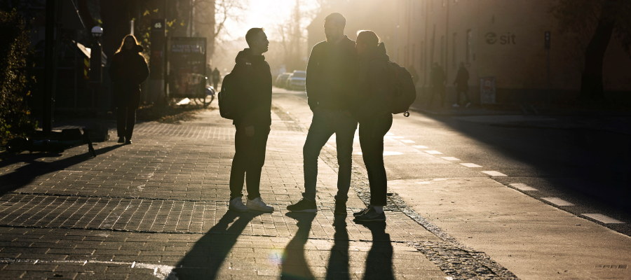 Siluett av tre studenter, en kvinne og to menn, utendørs, høst, motlys. Foto