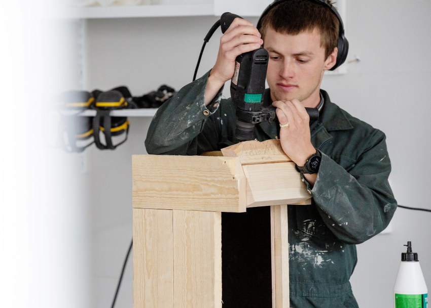 Lærerstudent jobber på verksted med planker og verktøy. foto